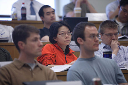 A group of people seated in a lecture hall, attentively listening and taking notes.